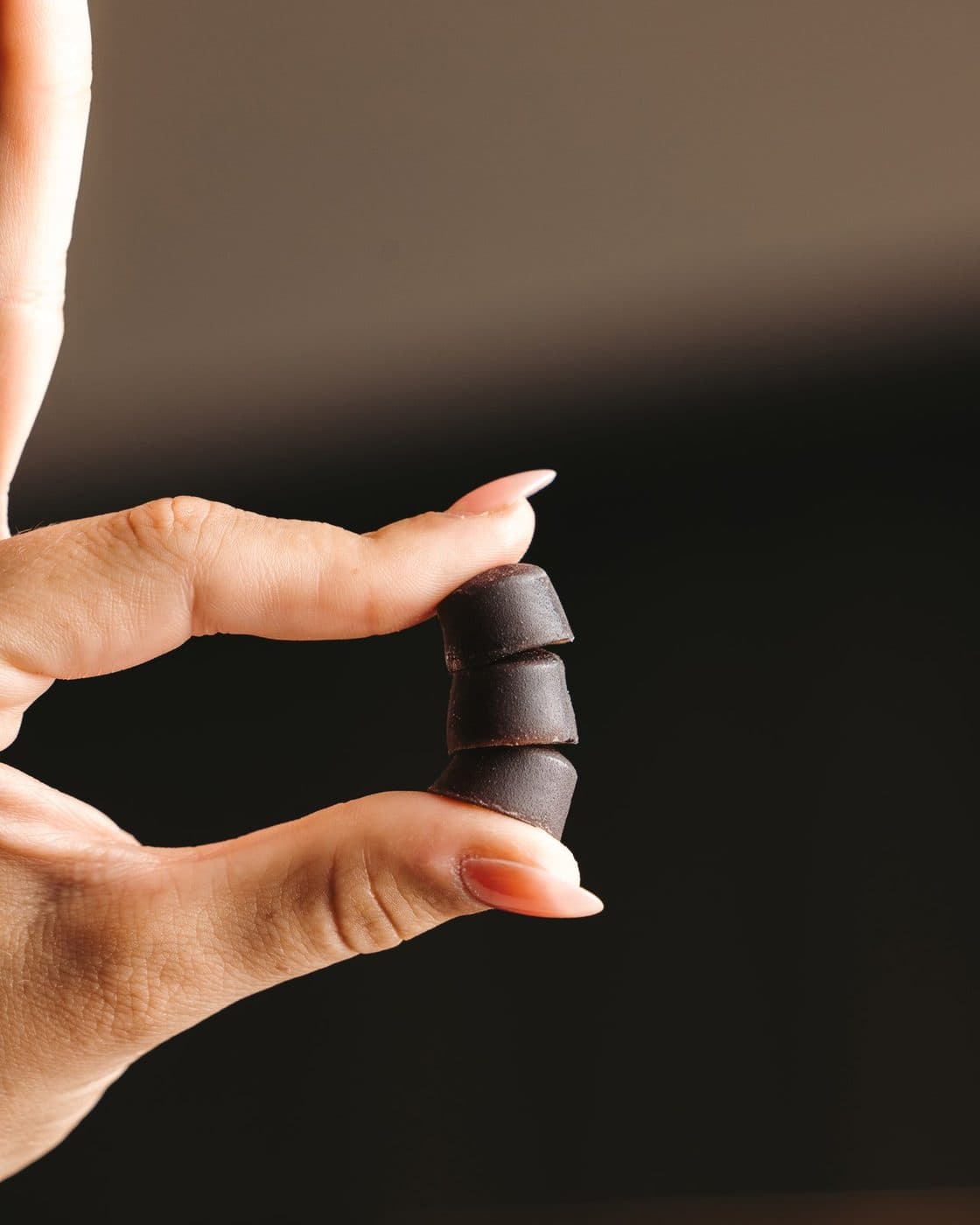 A hand holding a stack of three BioCandy PrimaVie Shilajit gummies