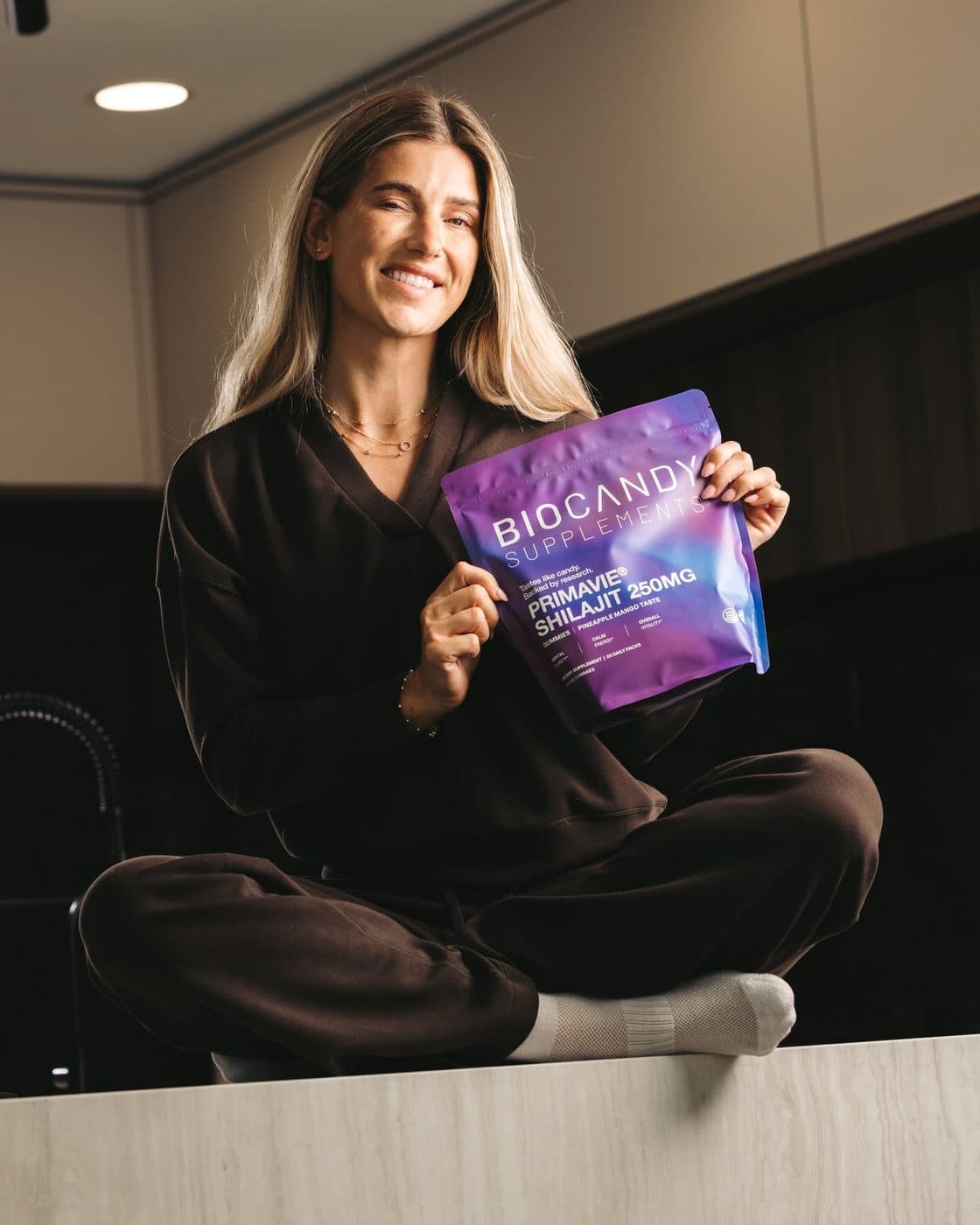 A woman smiling while holding a BioCandy PrimaVie Shilajit pouch